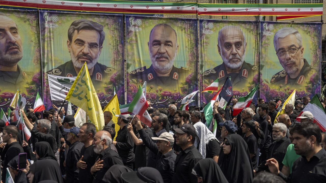 People hold flags near posters displaying assassinated IRGC military leaders during a state funeral service in Enqelab Square on June 28, 2025, in Tehran, Iran.