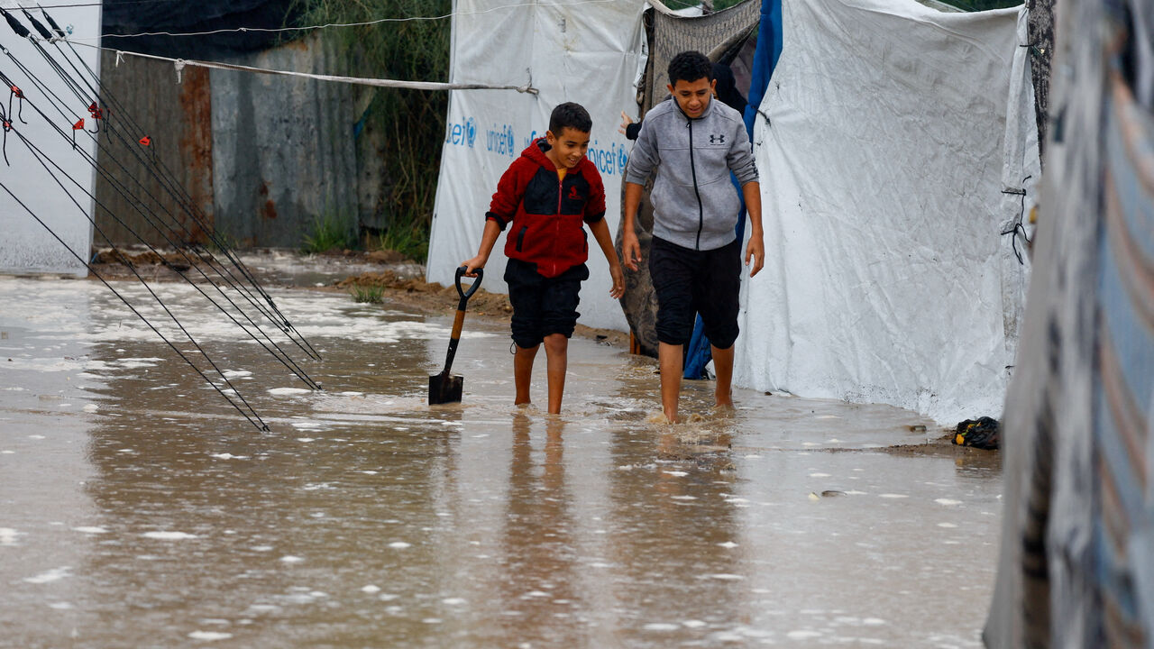 Displaced Palestinians walk through rainwater as they shelter in a flooded tent camp on a rainy day in Nuseirat, central Gaza Strip, December 12, 2025. REUTERS/Mahmoud Issa