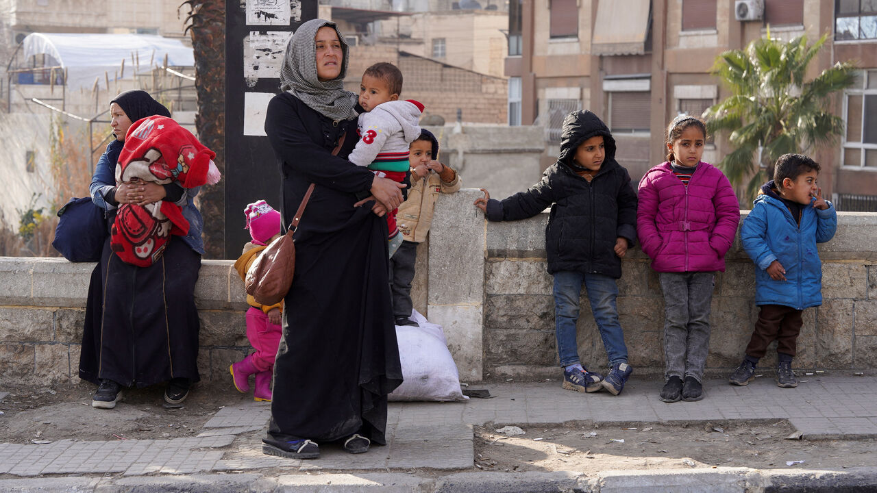 A woman carries her child as she flees, following renewed clashes between the Syrian army and the Syrian Democratic Forces (SDF), in Aleppo, Syria, January 7, 2026. REUTERS/Karam al-Masri
