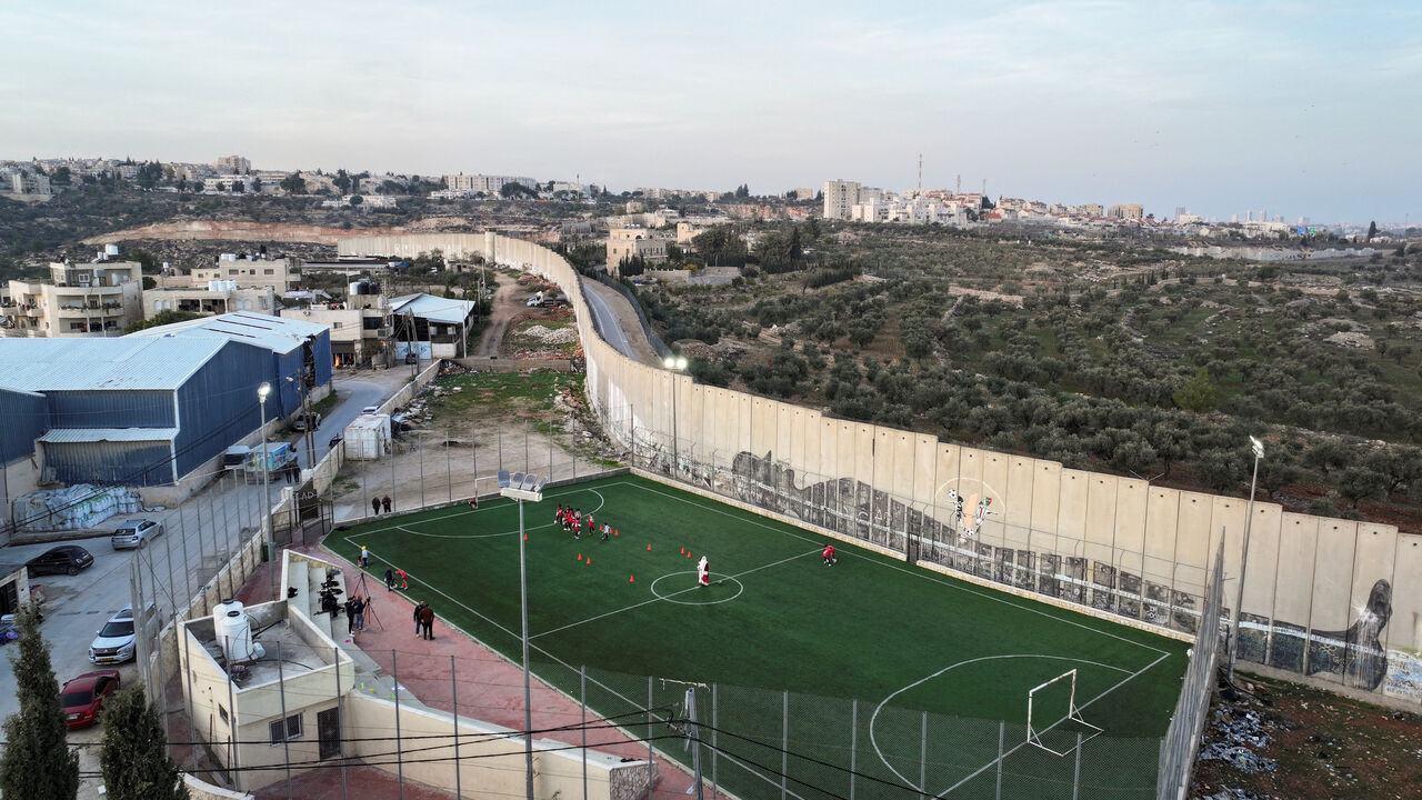 Drone view shows a man dressed as Santa playing football with Palestinian teens next to West Bank barrier separating Aida refugee camp from Jerusalem, in the Israeli-occupied city of Bethlehem, December 22, 2025. REUTERS/Ammar Awad