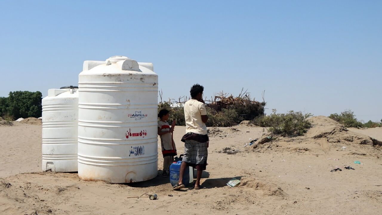 People standing next to water tanks at Al Salam camp for the internally displaced in Aden
