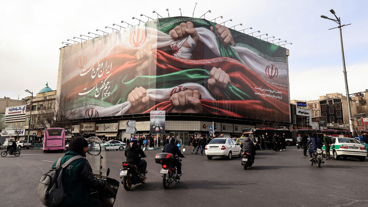 Vehicles pass by a large patriotic banner depicting the Iranian flag on Enghelab Square in Tehran on January 14, 2026. 