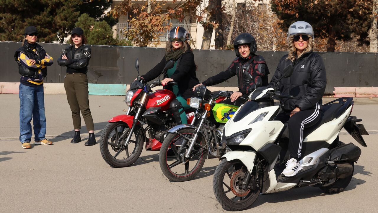 Iranian instructor Maryam Ghelich stands with student Narghes as they look at Elham (3rd R), Leila and Mona, posing on their motorbikes before their lesson at a training center in northern Tehran on Dec. 7, 2025.