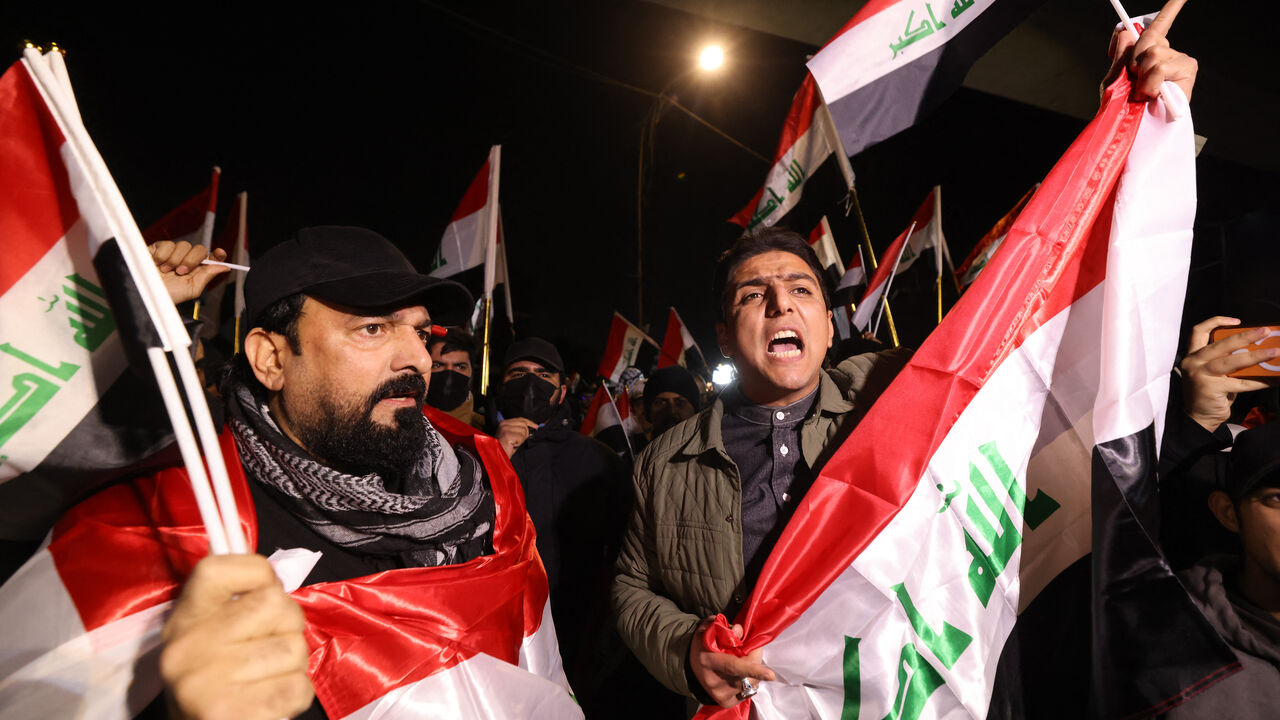 Iraqis raise their flags during a protest at the entrance to the Hanging Bridge, one of the entrances to the Green Zone in Baghdad on Jan. 28, 2026.  