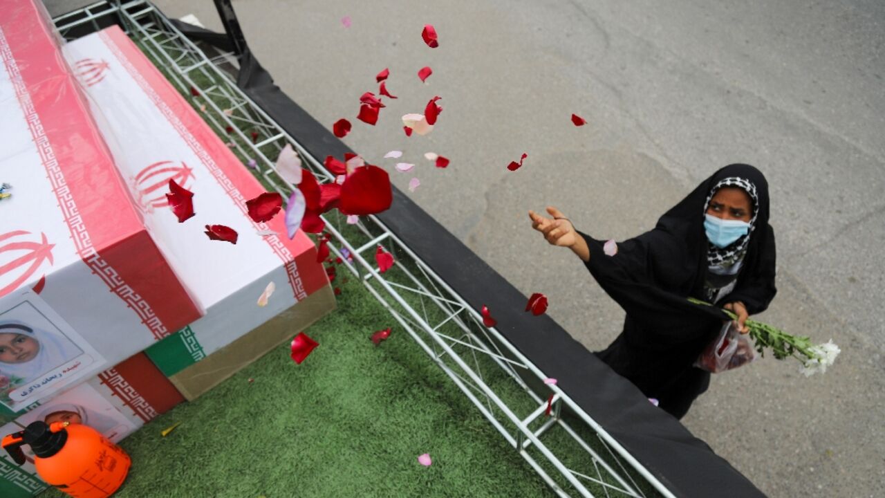 In this handout picture from Iranian state media, a mourner tosses flower petals on the coffins of children who were killed in a reported strike on a primary school in Iran’s Hormozgan province during a funeral
