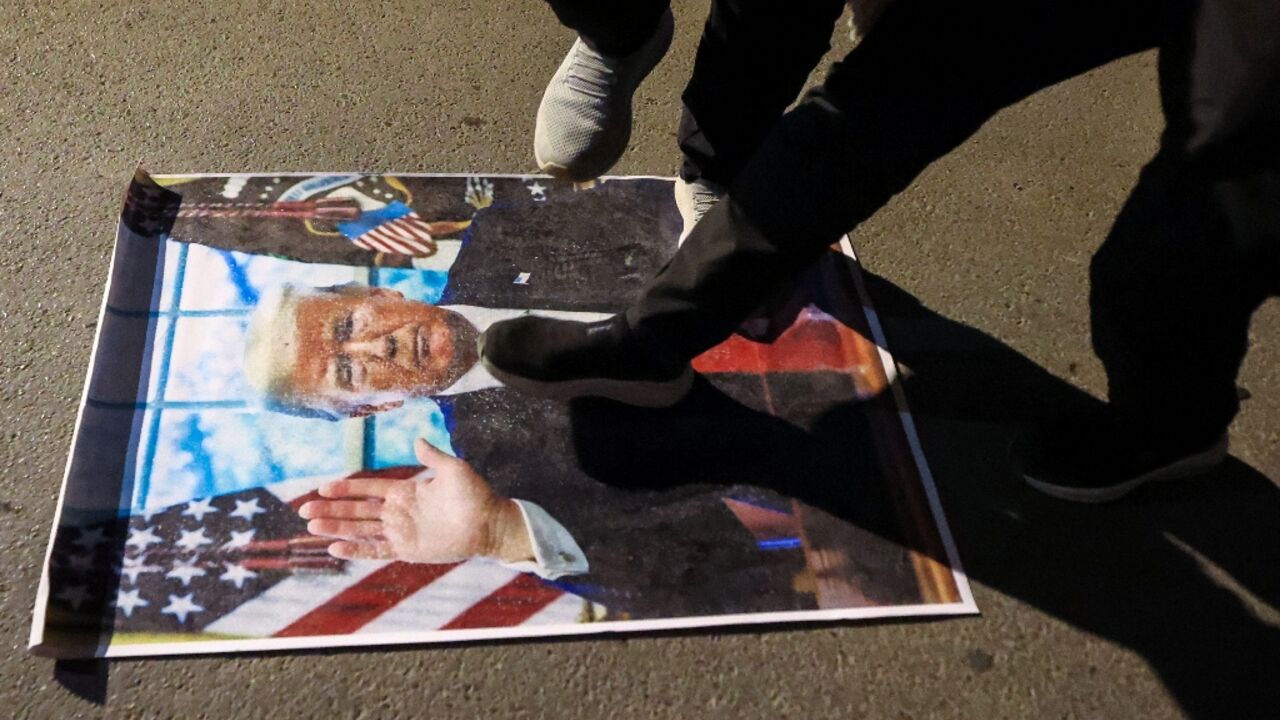 Demonstrators against the war in Iran trample on a portrait of US President Donald Trump during a protest as they march toward the US embassy in Baghdad