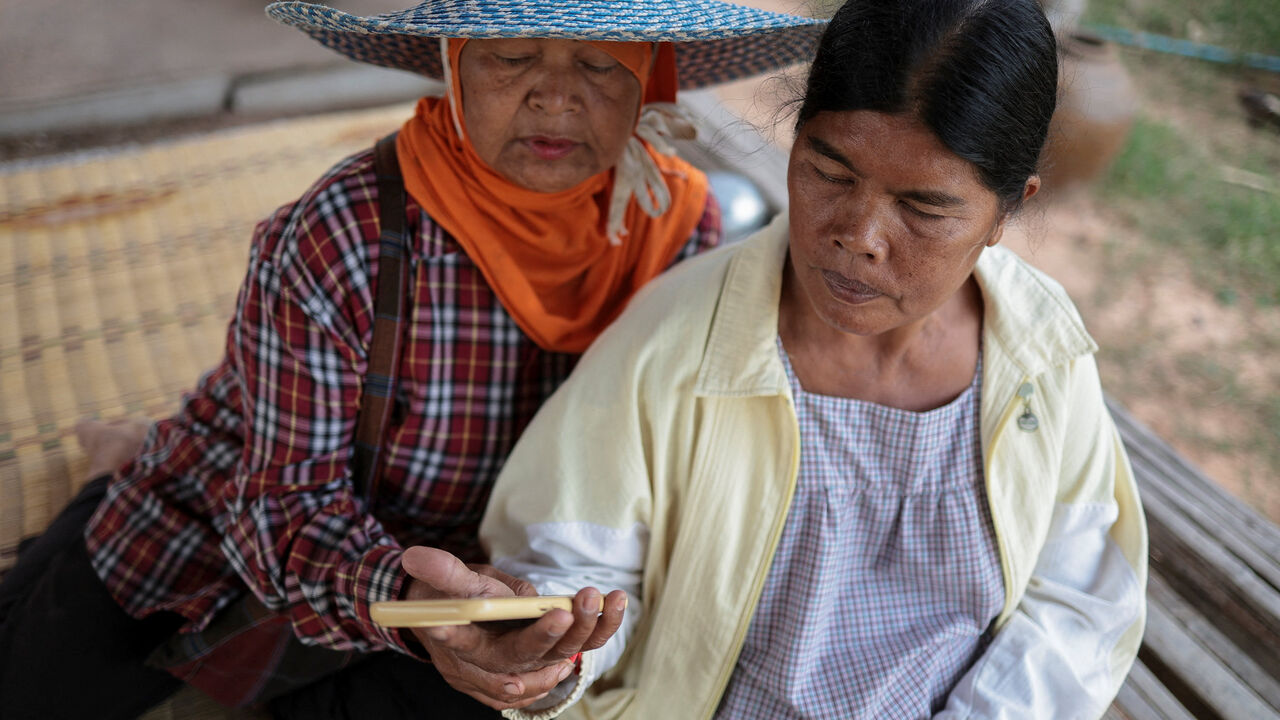 Sommai Butdee, 58, looks at her mobile phone with her friend Laaiad Namneewong, 62, as they wait for news of Sommai's nephew, Panupong Muentan, 27, an engine room mechanic and one of three Thai crew members who remain missing after a Thai ship was hit by unknown projectiles in the Strait of Hormuz, amid the U.S.-Israel conflict with Iran, at her home in Ban Sai village, in Surin province, Thailand, March 13, 2026. REUTERS/Chalinee Thirasupa