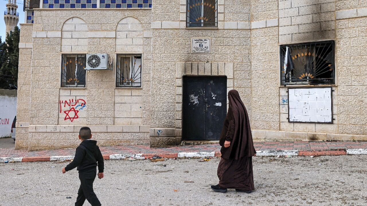 A Palestinian woman and boy walk past offensive Hebrew graffiti on the walls of a damaged house  age in the occupied West Bank
