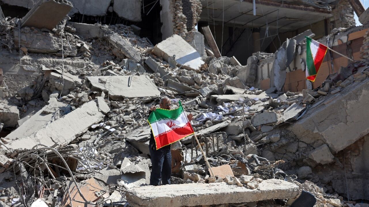 A man holds an Iranian flag amid the debris of a destroyed building following airstrikes in central Tehran on March 4, 2026