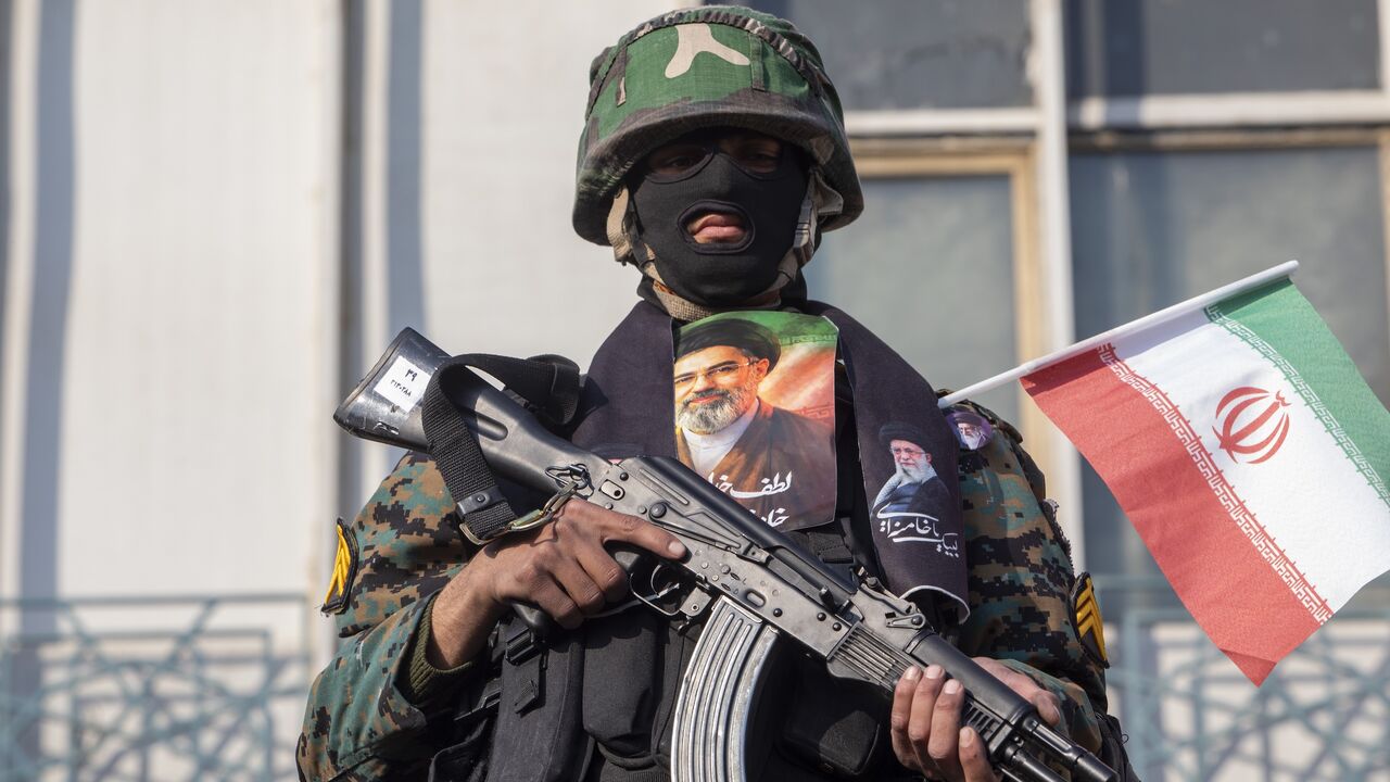 A security forces member with a picture of Iran's new supreme leader, Ayatollah Mojtaba Khamenei, watches over demonstrators as they gather for a rally in support of the new supreme leader at Enghelab Square on March 9, 2026 in Tehran, Iran. 