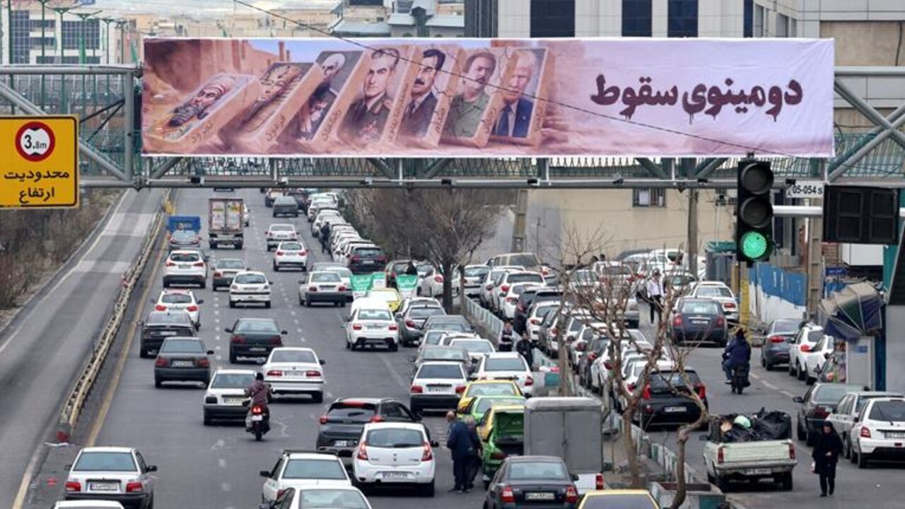Traffic rolls along a main throughfare under a banner with images of past and present leaders that reads in Farsi, "Domino fall," in the Iranian capital, Tehran, on Jan. 19, 2026. — ATTA KENARE / AFP via Getty Images