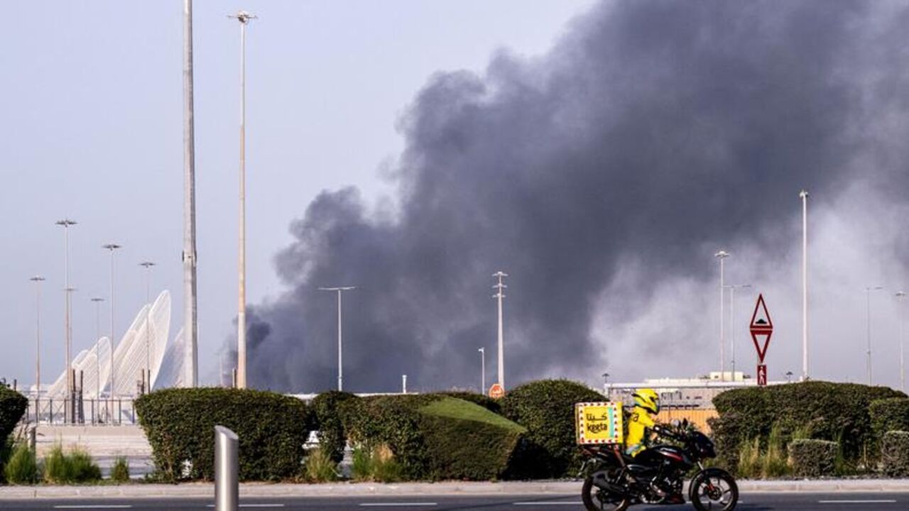 A food delivery driver rides close to a plume of smoke rising from the Zayed Port following a reported Iranian strike in Abu Dhabi, on March 1, 2026. — Ryan Lim / AFP via Getty Images