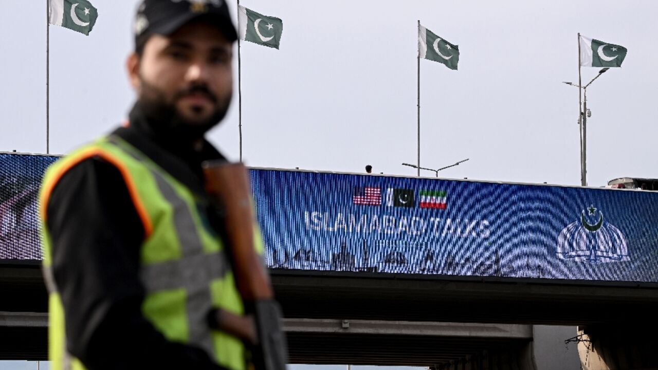 A policeman stands guard in front of a digital screen displaying news of US–Iran peace talks along a road in Pakistan's capital Islamabad