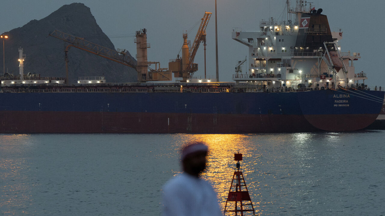 FILE PHOTO: A man sits on the waterfront as a vessel sits at anchor inside Sultan Qaboos Port, amid the U.S.-Israeli conflict with Iran, in Muscat, Oman, March 20, 2026. REUTERS/Stelios Misinas/File Photo