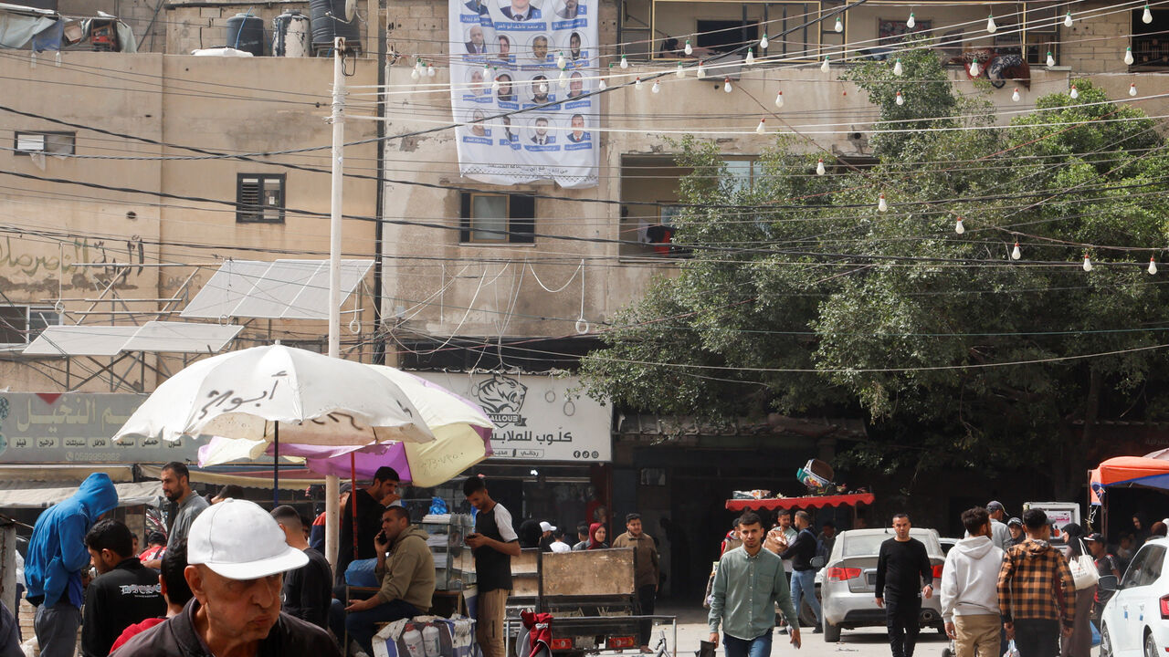 Palestinians walk past an electoral candidates list displayed in Deir al-Balah, central Gaza Strip, April 18, 2026. REUTERS/Haseeb Alwazeer