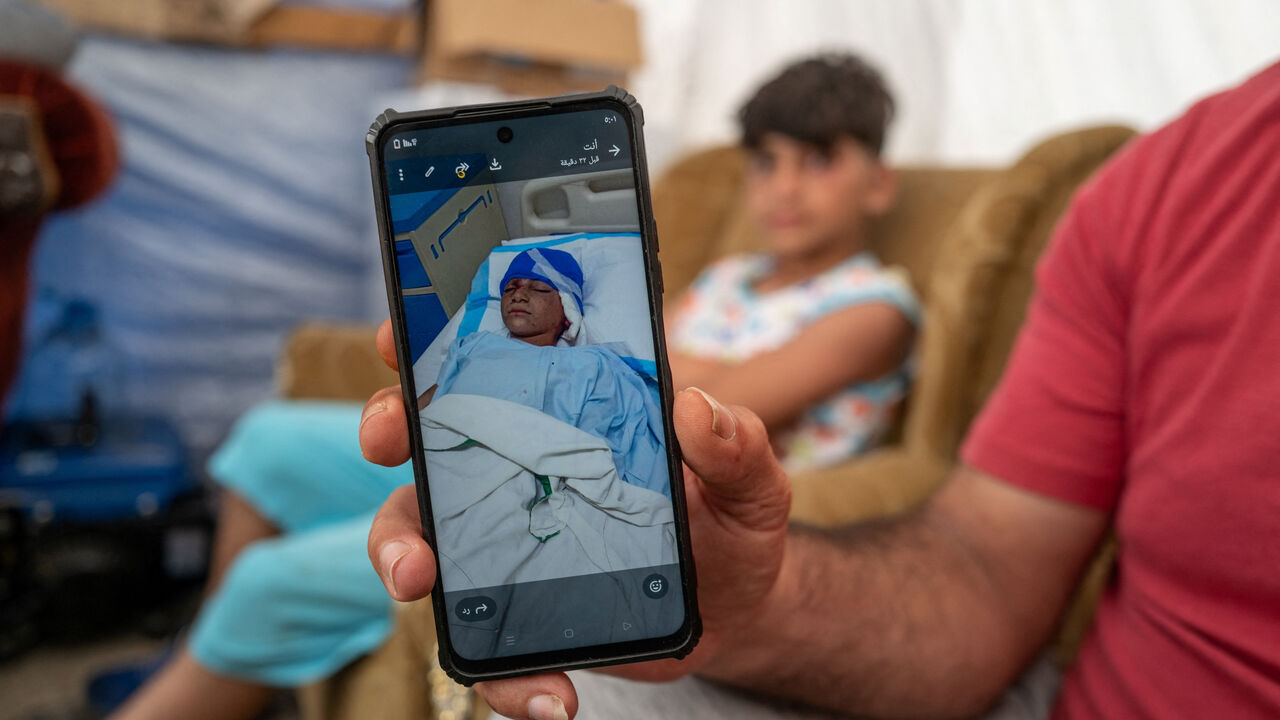 Rabih Khreisse, 44, a displaced Lebanese man from the southern village of Khiyam, near the border with Israel, shows a photograph of his son Ziad, 11, lying in a hospital after being wounded in an Israeli strike in 2024, as they sit at their shelter in a makeshift encampment, amid a temporary ceasefire between Lebanon and Israel, in Beirut, Lebanon April 27 2026. REUTERS/Zohra Bensemra