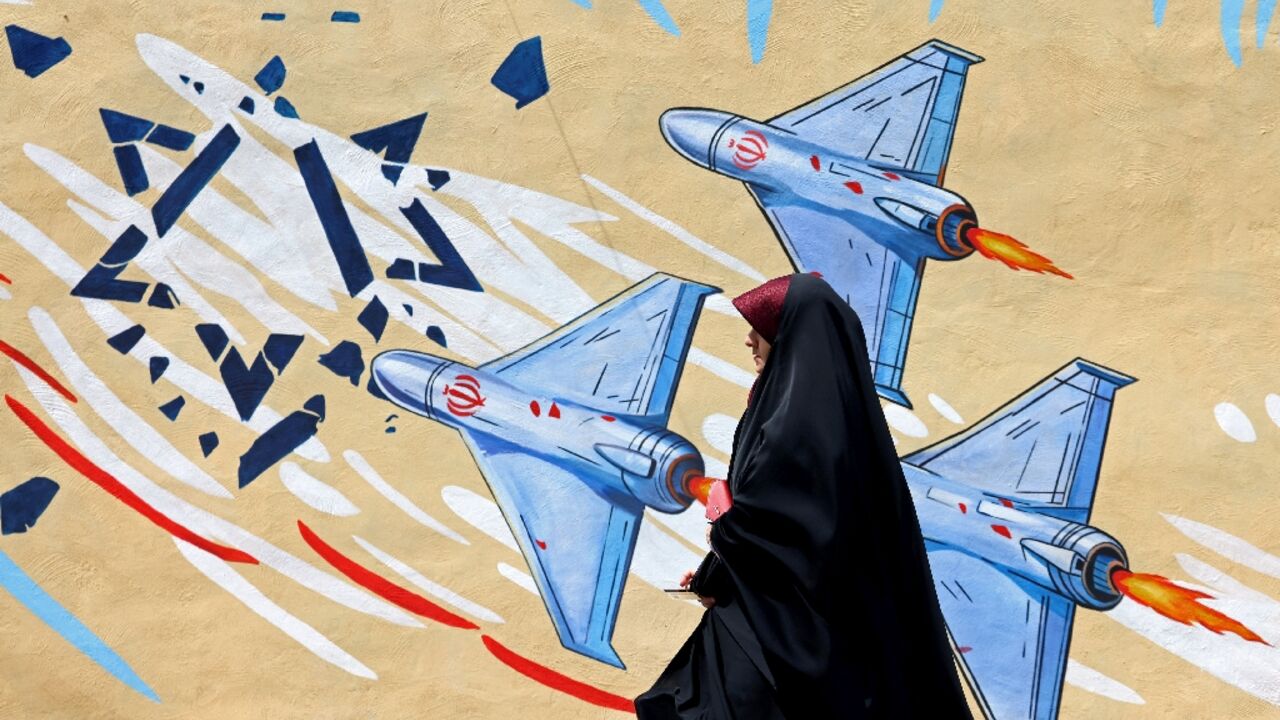 A woman walks past an anti-US and anti-Israel mural in Tehran