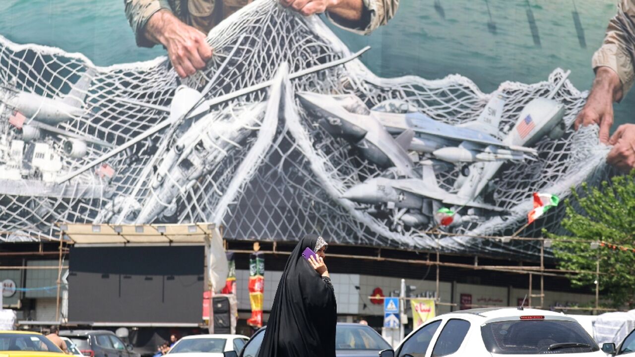 A woman walks past a giant billboard in Tehran that reads 'the Strait of Hormuz remains closed.'