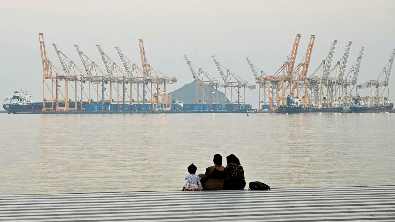 A family sits against the backdrop of a dockyard in Khor Fakkan in the Gulf emirate of Sharjah, off the coast of the Gulf of Oman, on Feb. 25, 2026. 
