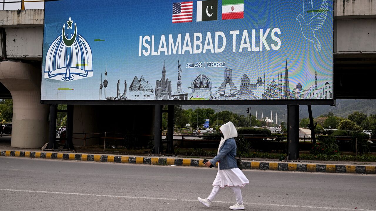 A woman walks past a digital screen displaying news of US-Iran peace talks along a road in Islamabad on April 10, 2026. 