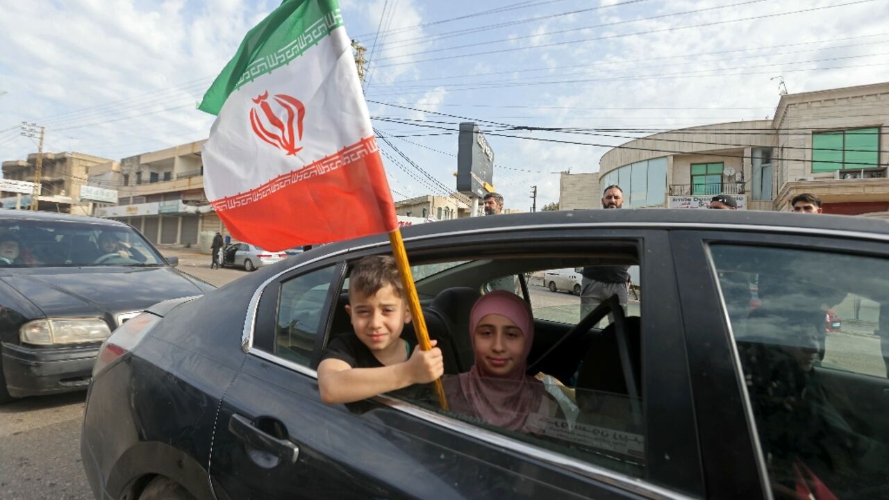 A boy holds an Iranian flag as he returns back to the southern Lebanese town of Marwanieh