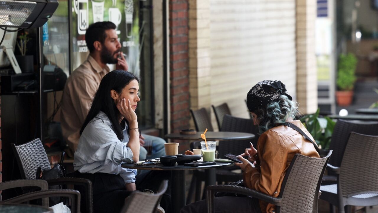 Two women sit at a cafe table with drinks in Tehran