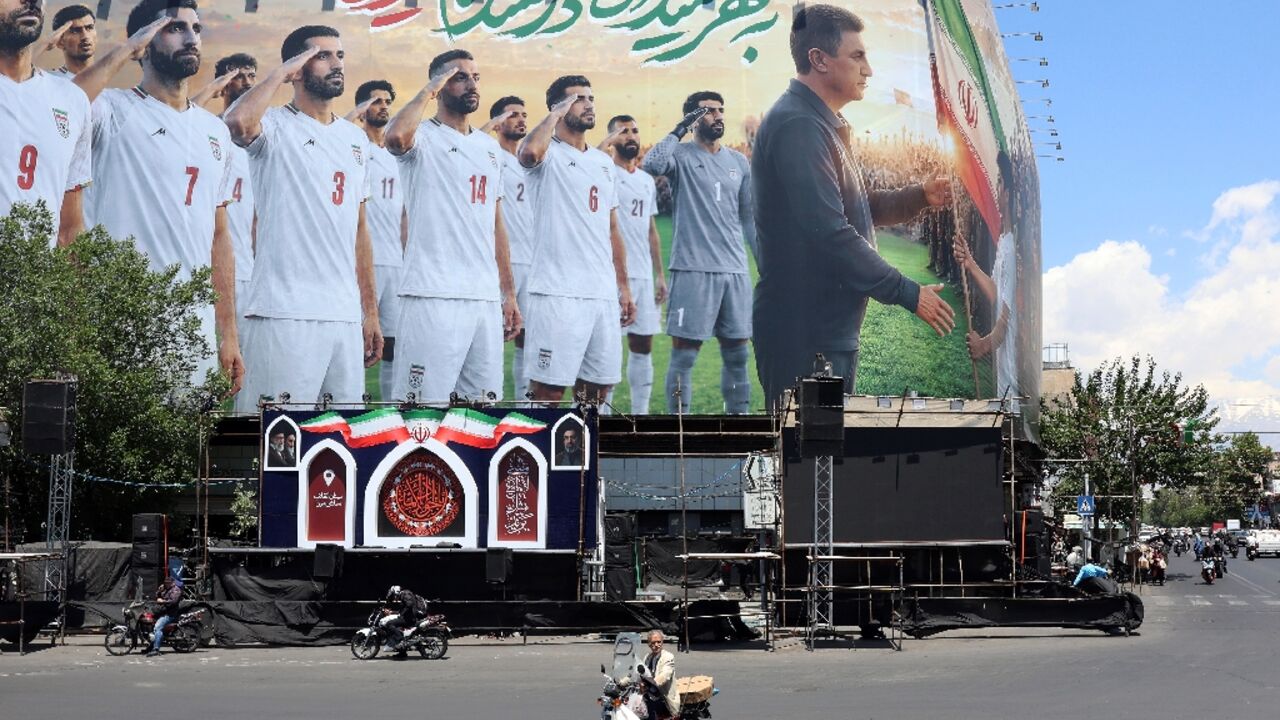 Tehran residents on motorbikes ride past a billboard supporting Iran's national football team in the upcoming 2026 World Cup