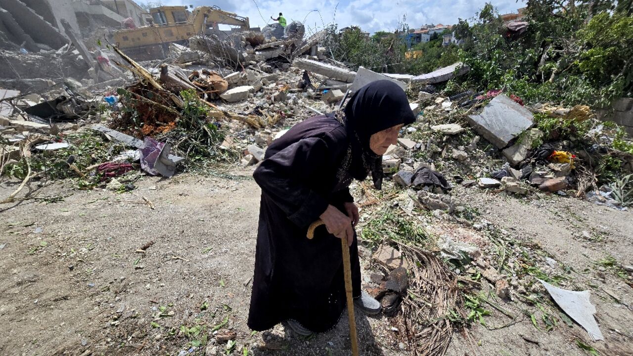 A woman walks past Lebanese rescuers searching through the rubble in the southern village of Deir Qanun al-Nahr, a day after an Israeli strike