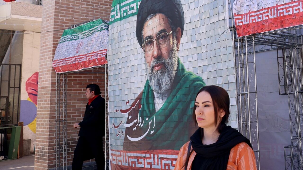 A woman walks past a large tiled image of Iran's current leader Ayatollah Mojtaba Khamenei outside a metro station in Tehran 