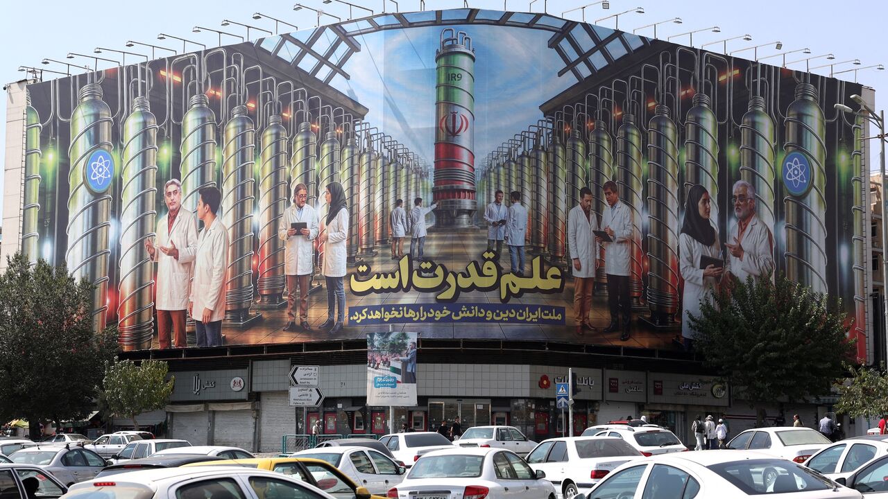 Iranians drive next to a billboard displaying pictures of nuclear scientists, centrifuges and a sentence reading in Farsi " Science is the power," at the Enqelab Square in Tehran, on Aug. 29, 2025. 