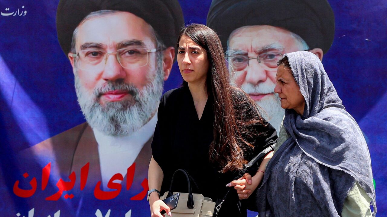 Women walk past a large banner depicting Iran's current supreme leader, Mojtaba Khamenei, and his predecessor and late father, Ali Khamenei, along a street in Tehran on May 6, 2026.