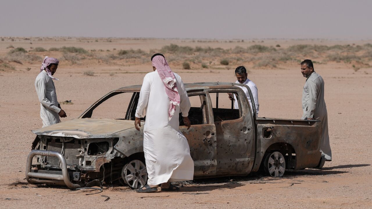 Men gather around the husk of a destroyed pickup truck that was driven by a local shepherd who was reportedly struck by Israeli forces and buried by locals at a grave nearby, in the Najaf desert in southwestern Iraq, on May 12, 2026. 