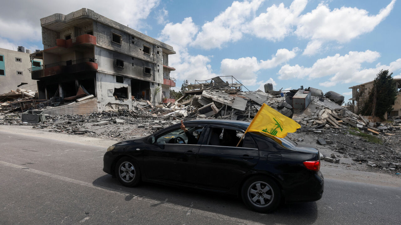 People display a Hezbollah flag from inside a car driving past rubble of destroyed buildings in Deir Qanoun al-Nahr, Tyre district, southern Lebanon,  June 15, 2026. REUTERS/Aziz Taher