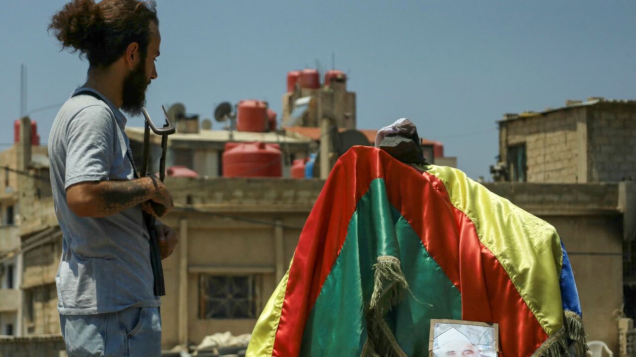 A Druze fighter stands at a roundabout draped with the Druze flag and a portrait of a local leader in the predominantly Druze city of Suwayda in southern Syria on July 21, 2025.