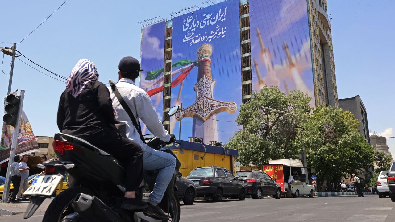 Motorists ride past a giant banner depicting Iranian missiles and a sword belonging to Imam Ali, the first Imam of the Shiites, at the Vanak Square in Tehran on June 10, 2026. 