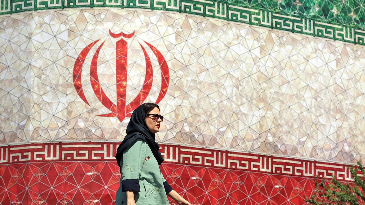 A woman walks past a billboard displaying Iran's national flag at Enghelab Square in Tehran on June 14, 2026.