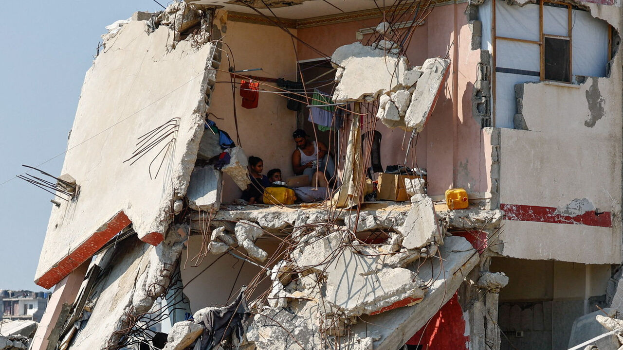 Palestinians sit inside a house damaged during the war, surrounded by destroyed buildings, in Gaza City, August 15, 2026. REUTERS/Mahmoud Issa