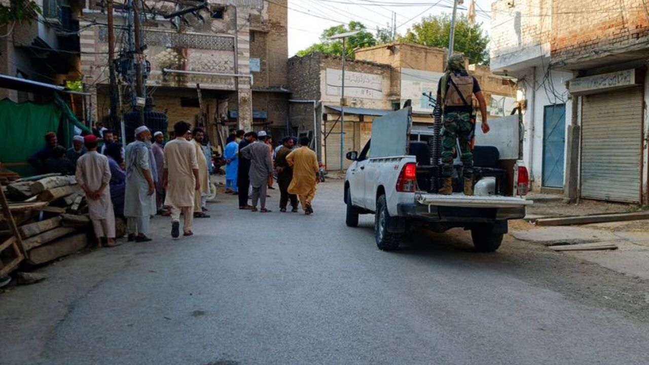 Residents and a police vehicle on a street following a suicide attack at a police facility in Kohat