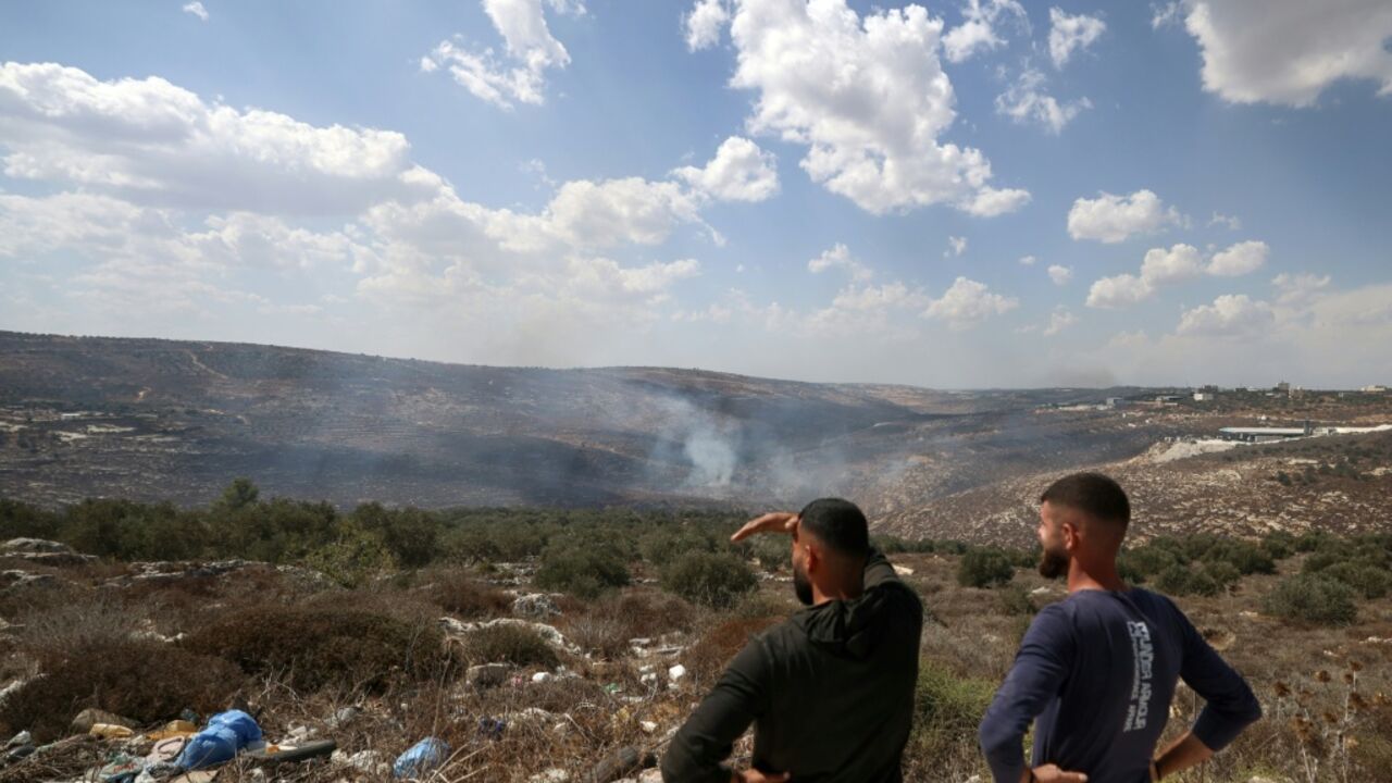 Palestinians stand on a hilltop looking down at the smoke from fires after Israeli soldiers fired tear gas at the olive harvest near the village of Asira al-Qibliya on October 3, 2026