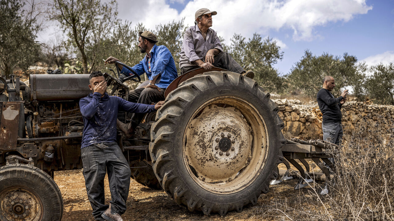 Palestinian men sitting in and by a tractor look on after another man was injured by gunfire whilst being chased away by Israeli forces, in Aqraba in the Israeli-occupied West Bank on Oct. 6, 2026.