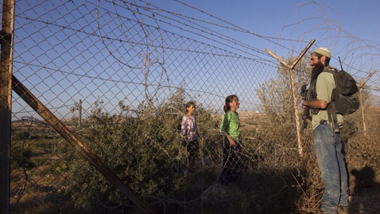 A Jewish settler participating in a drill held by the settler's security response teams, speaks to girls through a fence in the West Bank settlement of Kiryat Arba September 14, 2011. The drill simulated violence that could erupt ahead of the upcoming Palestinian bid for statehood at the United Nations. REUTERS/Ronen Zvulun (WEST BANK - Tags: POLITICS CIVIL UNREST)