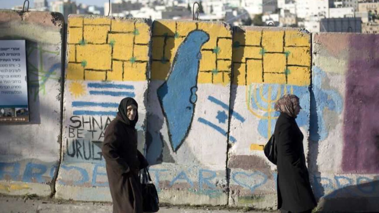 Palestinians walk past a blast wall with graffiti in Hebron Palestinians walk past a blast wall with graffiti in the West Bank city of Hebron January 13, 2013. Entrenched in what they view as their Biblical heartland, the hardline Jewish settlers of Hebron look forward with delight to next week's Israeli election. Picture taken January 13, 2013. To match ISRAEL-ELECTION/SETTLERS REUTERS/Baz Ratner (WEST BANK - Tags: POLITICS ELECTIONS)