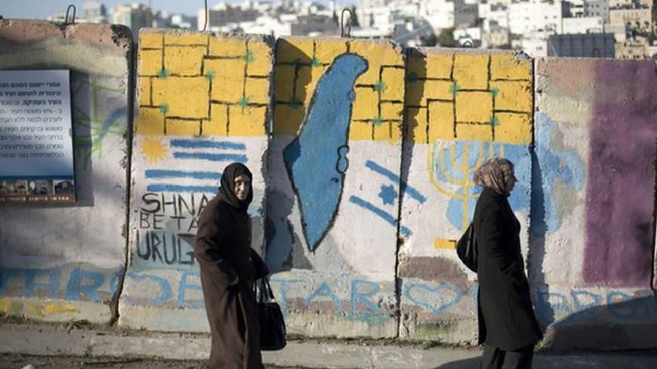 Palestinians walk past a blast wall with graffiti in Hebron Palestinians walk past a blast wall with graffiti in the West Bank city of Hebron January 13, 2013. Entrenched in what they view as their Biblical heartland, the hardline Jewish settlers of Hebron look forward with delight to next week's Israeli election. Picture taken January 13, 2013. To match ISRAEL-ELECTION/SETTLERS REUTERS/Baz Ratner (WEST BANK - Tags: POLITICS ELECTIONS)