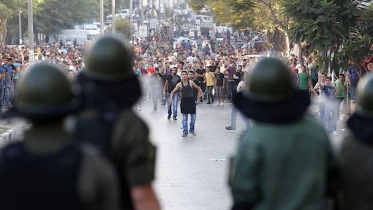 Palestinians security officers stand in front of protesters during clashes at a demonstration in Hebron Palestinians security officers stand in front of protesters during clashes at a demonstration against high living costs and the government in the West Bank city of Hebron September 10, 2012. Palestinian youths attacked a local police station and other government buildings in Hebron on Monday as protests against the rising cost of living in the occupied West Bank turned increasingly violent. REUTERS/Darren Whiteside (WEST BANK - Tags: POLITICS CIVIL UNREST) - RTR37S7M