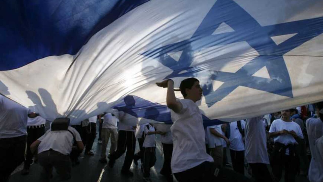 Israeli youths dance under a huge national flag during a parade marking Jerusalem Day in Jerusalem Israeli youths dance under a huge national flag during a parade marking Jerusalem Day in Jerusalem May 20, 2012. Jerusalem Day marks the anniversary of Israel's capture of the Eastern part of the city during the 1967 Middle East War. Israel annexed East Jerusalem as part of its capital in a move not recognized internationally. REUTERS/Baz Ratner (JERUSALEM - Tags: POLITICS ANNIVERSARY TPX IMAGES OF THE DAY) - RTR32D2U