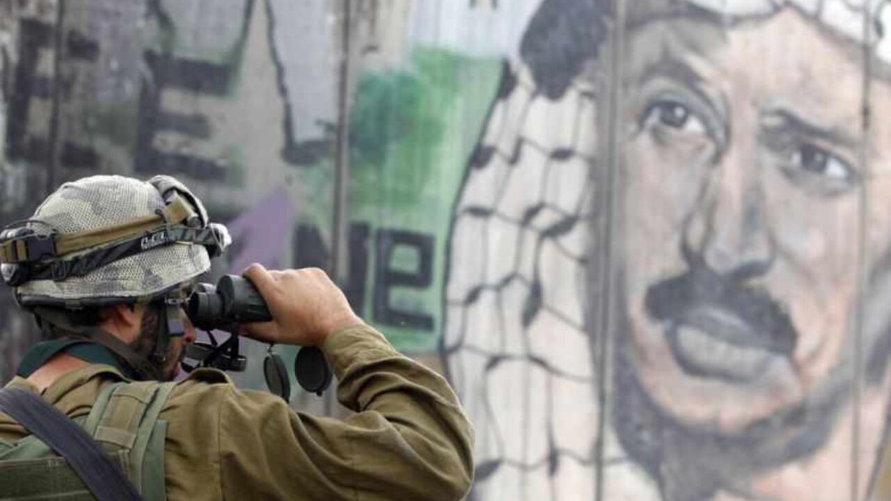 An Israeli soldier looks through binoculars during clashes with Palestinian stone-throwers near Ramallah An Israeli soldier looks through binoculars in front of a mural depicting the late Palestinian leader Yasser Arafat on the controversial Israeli barrier, during clashes with Palestinian stone-throwers at Qalandiya checkpoint near the West Bank city of Ramallah November 21, 2012. Clashes broke out between Palestinians and the Israeli army in multiple locations across the occupied West Bank on Wednesday, underlining heightened tensions by the Gaza conflict. REUTERS/Marko Djurica (WEST BANK - Tags: POLITICS CI