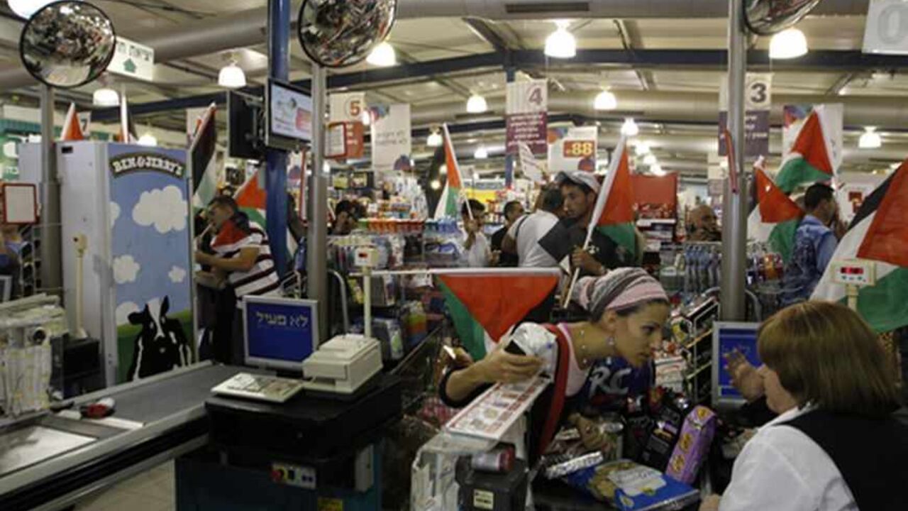 PALESTINIANS-ISRAEL/ An Israeli customer speaks with a cashier as foreign and Palestinian activists holding Palestinian flags march through a supermarket in the West Bank Jewish settlement of Modiin Illit October 24, 2012. Some 50 activists marched through the supermarket and tried to block a road in the settlement on Wednesday during a protest against Jewish settlements and in a call to boycott settlement products. REUTERS/Ammar Awad (WEST BANK - Tags: POLITICS CIVIL UNREST FOOD) - RTR39INJ