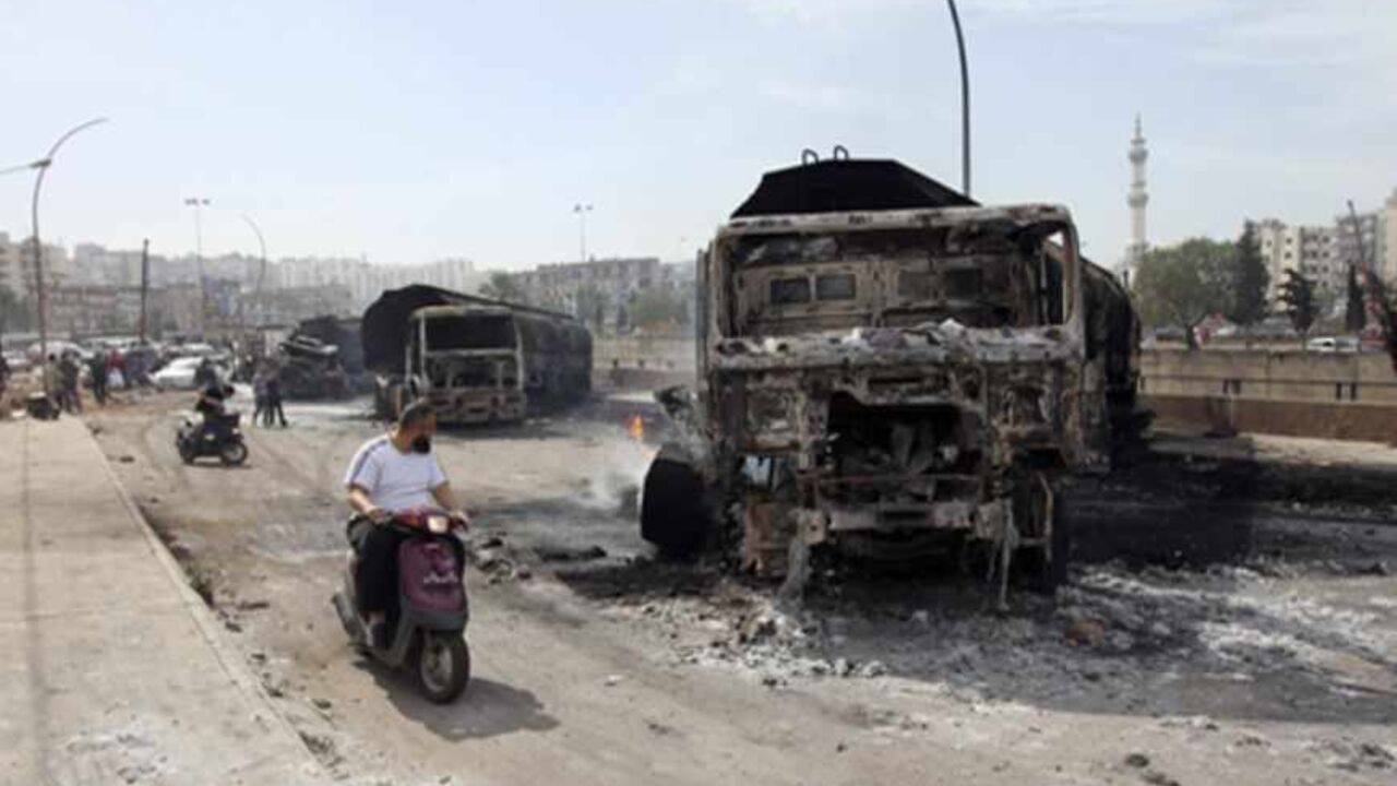 LEBANON/ A man rides his motorcycle near damaged fuel tanker trucks in Tripoli, northern Lebanon March 15, 2013. Seven Syria-bound fuel tanker trucks were burned and destroyed in Tripoli on Friday, according to the National News Agency. REUTERS/Omar Ibrahim (LEBANON - Tags: POLITICS CIVIL UNREST ENERGY) - RTR3F10L