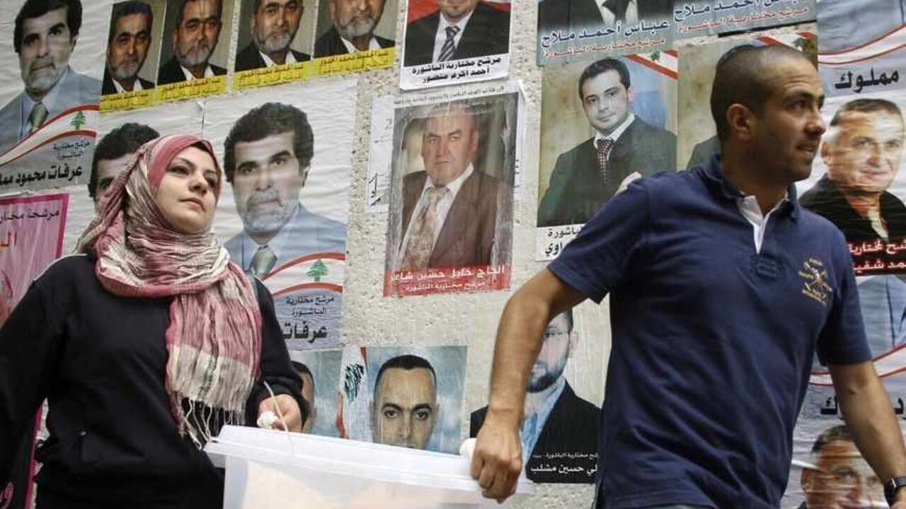 LEBANON/ Lebanese government election officials walk past a wall on which posters of Lebanese candidates running in the country's municipal election are pasted, as they carry a ballot box ahead of the country's municipal elections, in Beirut May 8, 2010. The voting is spread across four regions, each of which will vote on a Sunday in May. Beirut will be the second region to vote on Sunday, May 9, 2010. REUTERS/Mohamed Azakir (LEBANON - Tags: ELECTIONS POLITICS) - RTR2DLXT