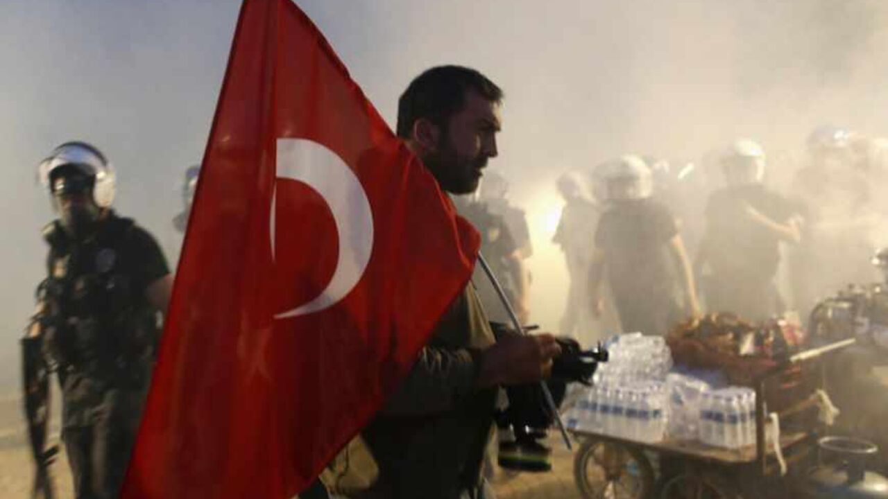 A protester holds a Turkish flag as riot police order them to evacuate Gezi Park in central Istanbul A protester holds a Turkish flag as riot police order them to evacuate Gezi Park in central Istanbul June 15, 2013. Thousands of people took to the streets of Istanbul overnight on Sunday, erecting barricades and starting bonfires, after riot police firing teargas and water cannon stormed a park at the centre of two weeks of anti-government unrest. Lines of police backed by armoured vehicles sealed off Taksim Square in the centre of the city as officers raided the adjoining Gezi Park late on Saturday, where